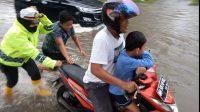 Ditengah Hujan dan Banjir, Kasat Lantas Polres Dumai Dorong Motor dan Seberangkan Pelajar Sekolah